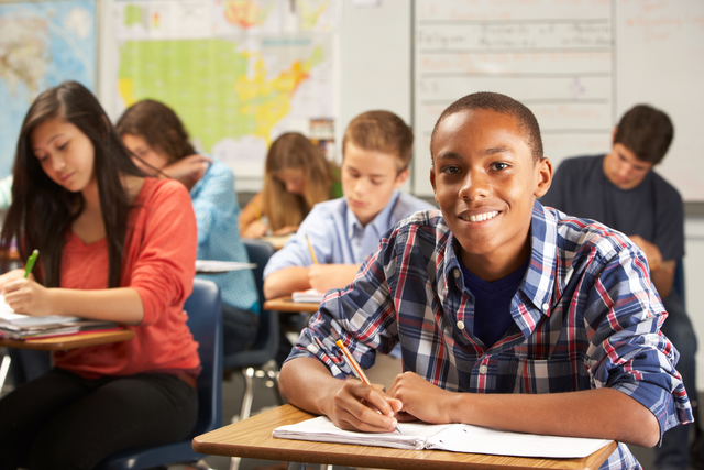 A variety of middle-school age students take a test in a classroom.