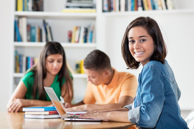 A young female student sits at a desk on her computer. 