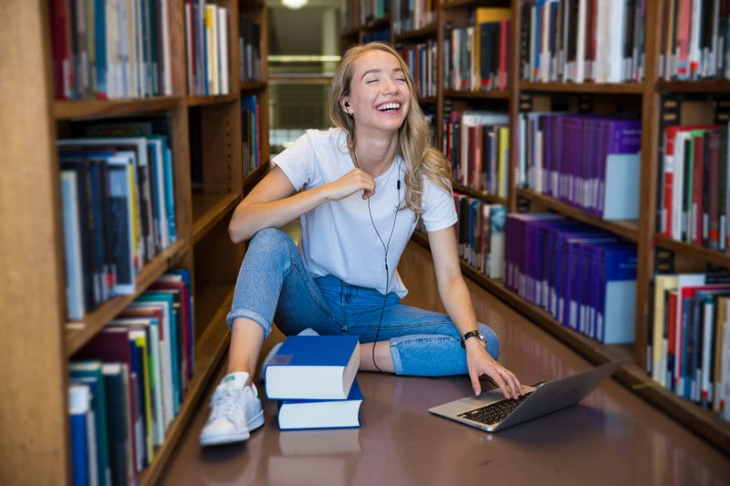 College student enjoying studying with computer in library stacks.